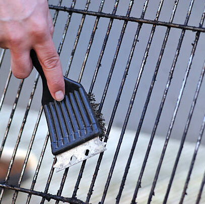 human hand is cleaning the grill rost with scrubber